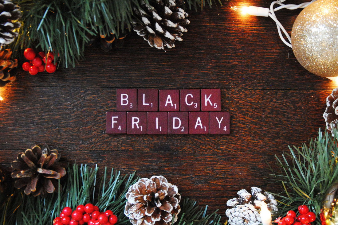 Black Friday scrabble tiles sitting on wood surrounded by pine cones and Christmas lights and ornaments