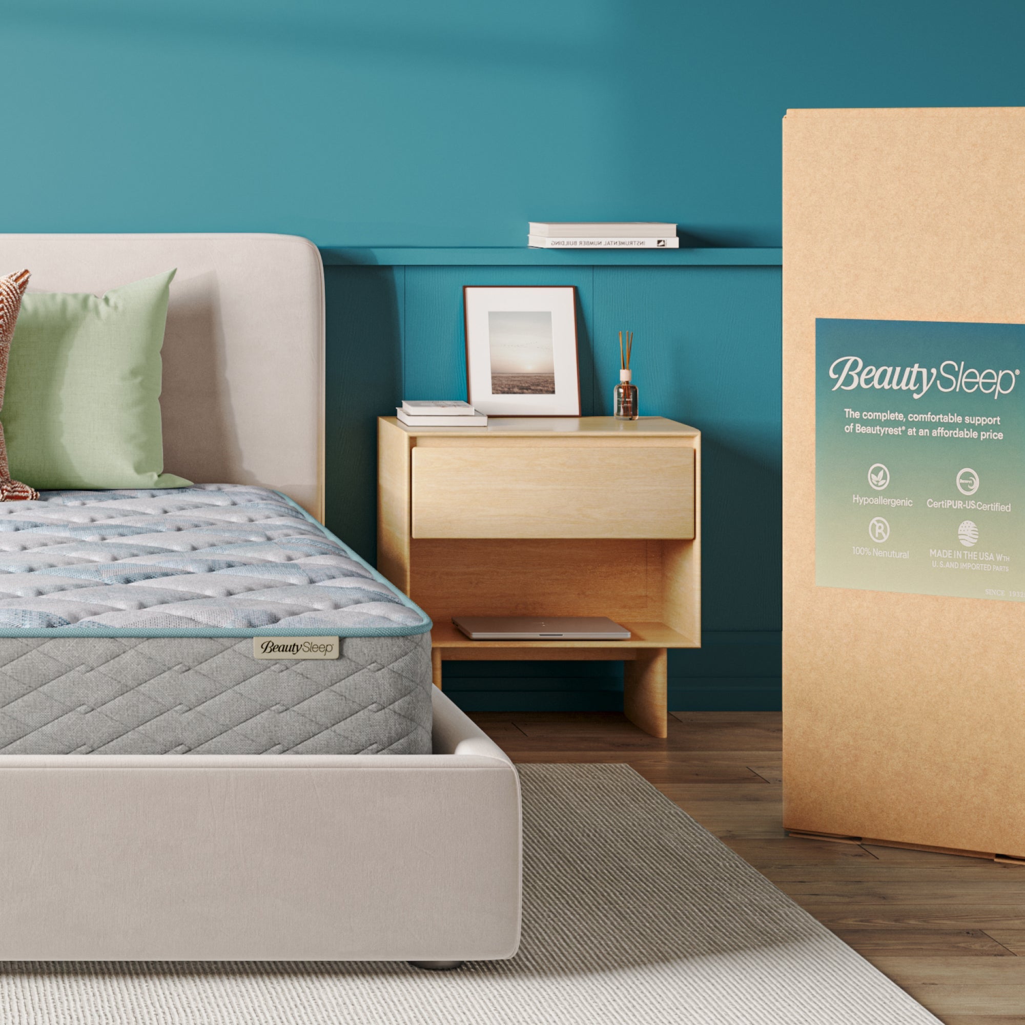 Beautysleep Mattress in a grey bedframe with 3 pillows on top of it within a bedroom setting with BeautySleep packaging to the right of it.