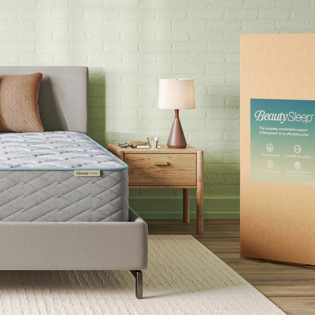 Beautysleep Mattress in a grey bedframe with 3 pillows on top of it within a bedroom setting with BeautySleep packaging to the right of it.