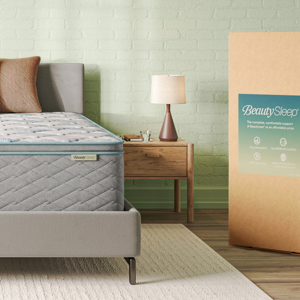 Beautysleep Mattress in a grey bedframe with 3 pillows on top of it within a bedroom setting with BeautySleep packaging to the right of it.