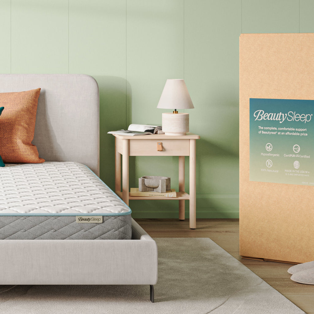 Beautysleep Mattress in a grey bedframe with 3 pillows on top of it within a bedroom setting with BeautySleep packaging to the right of it.