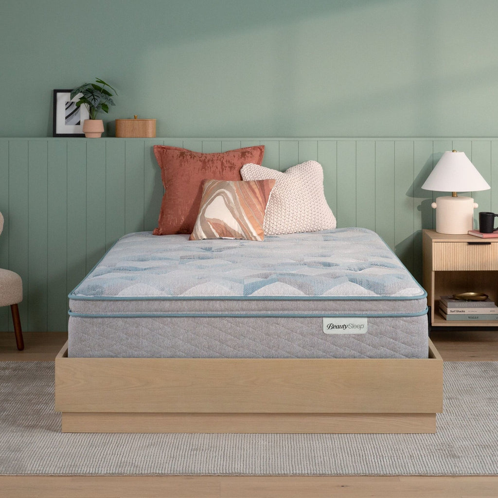 Beautysleep by Beautyrest mattress in a brown bedframe in a room setting with a lamp and nightstand.