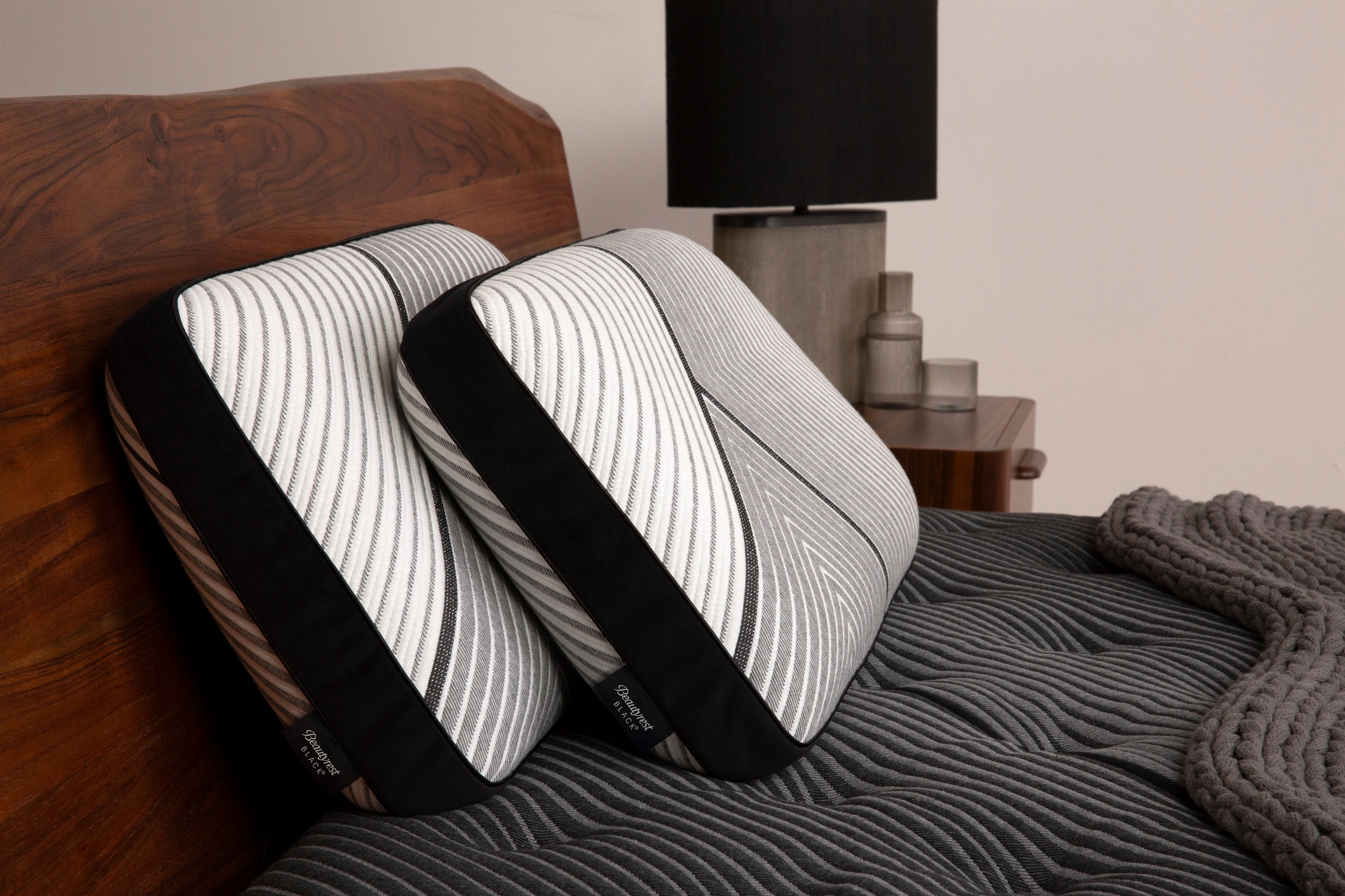 Two Beautyrest Black Black pillows sitting against a brown headboard and sitting on beautyrest black mattress