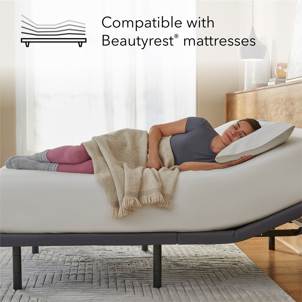 Woman lying on a Beautyrest mattress on top of a Pearl adjustable base with a pillow, surrounded by a blanket, in a bedroom setting.